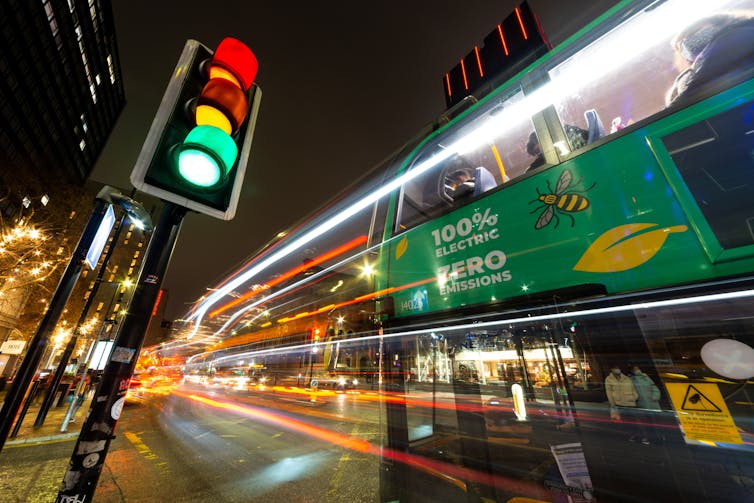 A long exposure image of a zero-emission bus passing a traffic light.