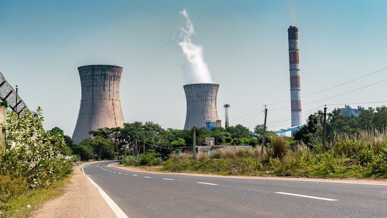 A road winding through vegetation with cooling towers in the distance.