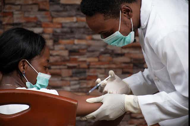 Un homme portant le masque en train de vacciner au bras une femme portant le masque