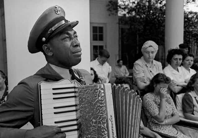 A black man dressed a military uniform is crying a he plays the accordion