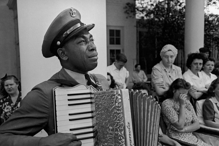 A black man dressed a military uniform is crying a he plays the accordion