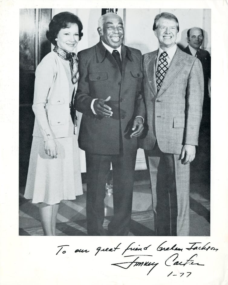 An elderly black men is standing between a smiling white man and a white women.