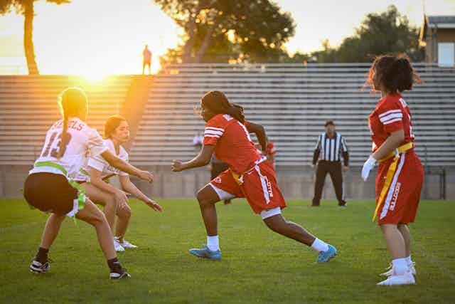 High school girls in sports uniforms play flag football on stadium field