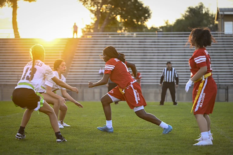 High school girls in sports uniforms play flag football on stadium field