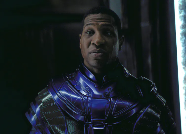 Kang stands against a black backdrop wearing a shiny purple suit.