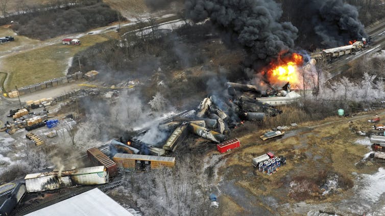Train cars after the derailment are jumbled and on fire.