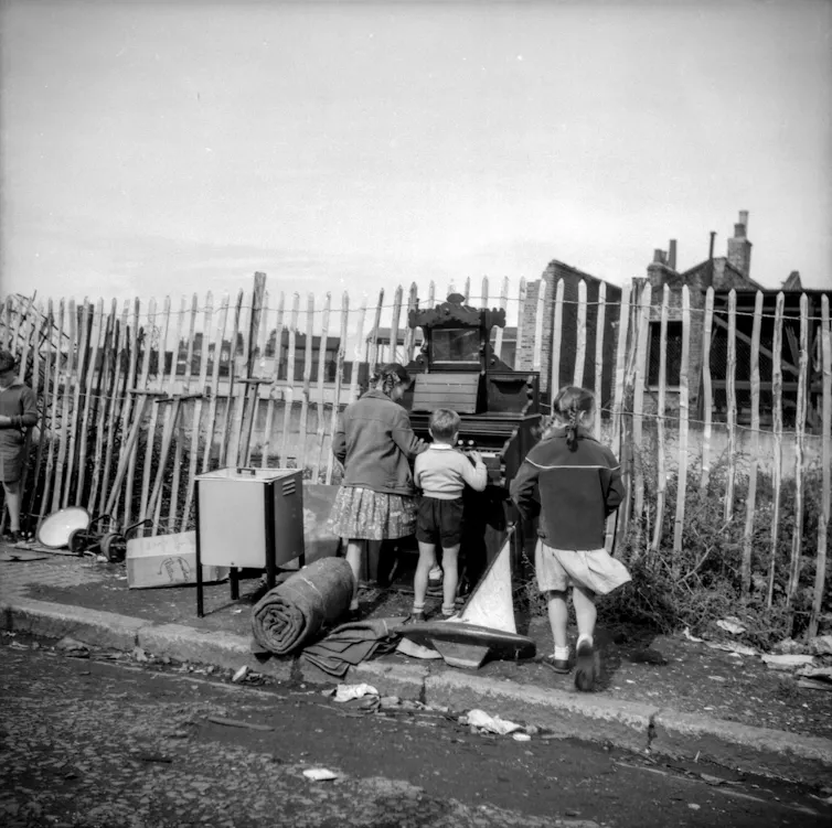 A black and white shot of three children and an organ outside.