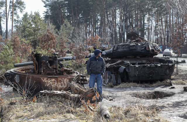 A Ukrainian civilian stands looking at a Russian tank destroyed in the fighting. 