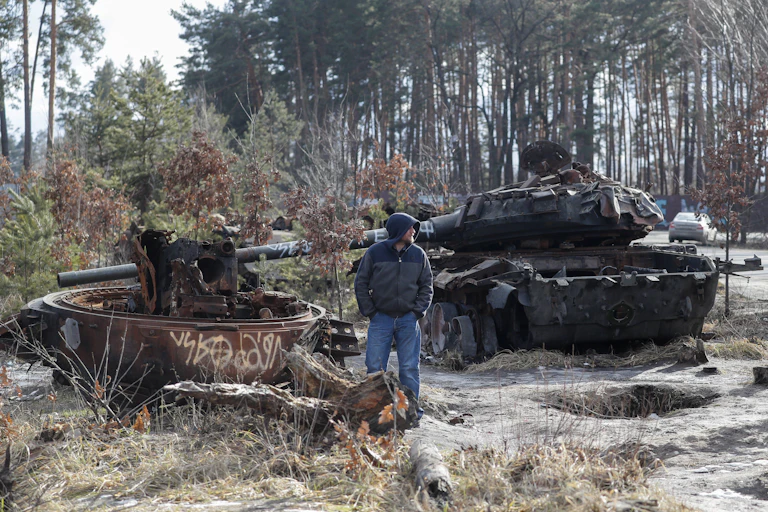 A Ukrainian civilian stands looking at a Russian tank destroyed in the fighting.