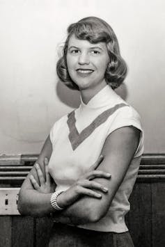 A young woman smiling at the camera with her arms folded.