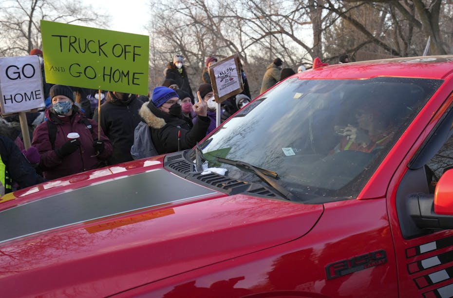 A pick up truck drives passed people carrying signs that read: truck off, go home.