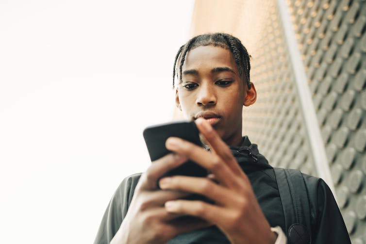 a black teenage boy looks at a smart phone he's holding in both hands