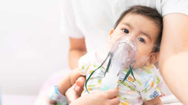 Toddler in father's arms being treated for respiratory illness with mask