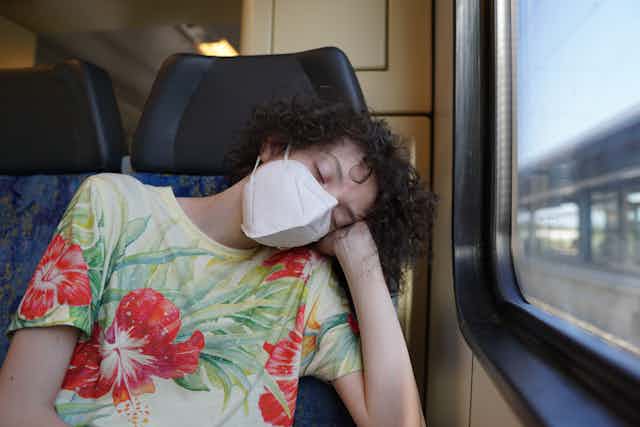 Man asleep on train wearing face mask