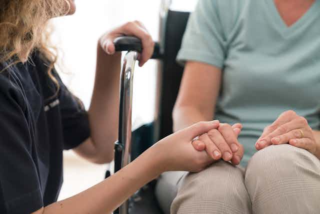 person kneeling holds hand of someone in wheelchair