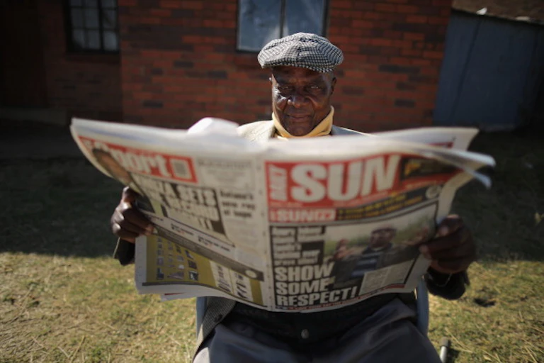 A man sits outside his Soweto home and reads the Daily Sun newspaper.