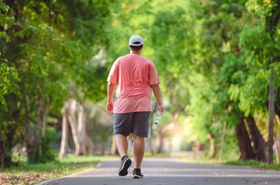 A man wearing workout clothes goes for a walk or jog in a sunny park.