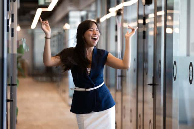 A young woman in professional attire cheers and smiles in an office