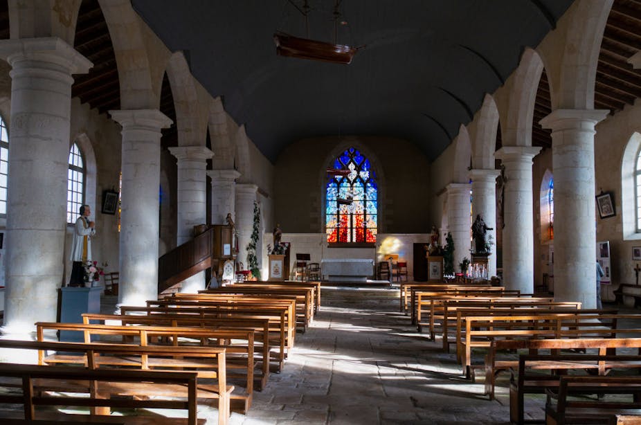 View of a church altar and pillars with empty wooden pews, taken from the back of a sanctuary.