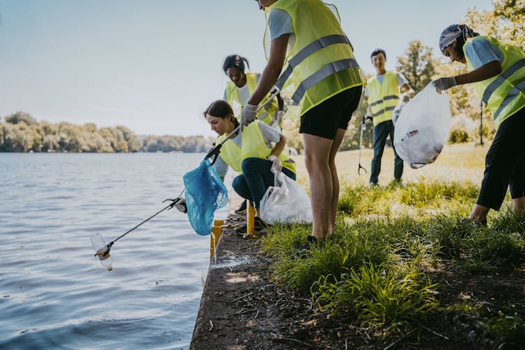 A handful of people in bright yellow vests fetch garbage out of a waterway.