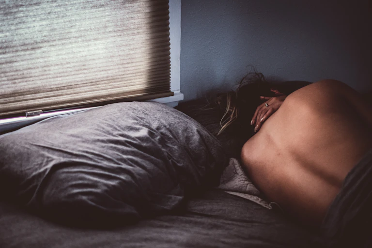 woman lying in bed, alone, back to viewer, a ring on her hand