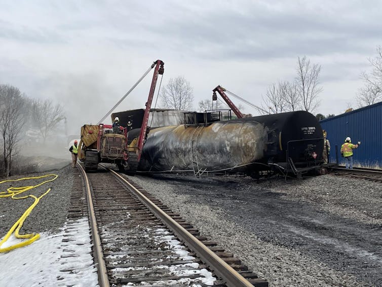 Cranes work to move burned train cars off the rails.