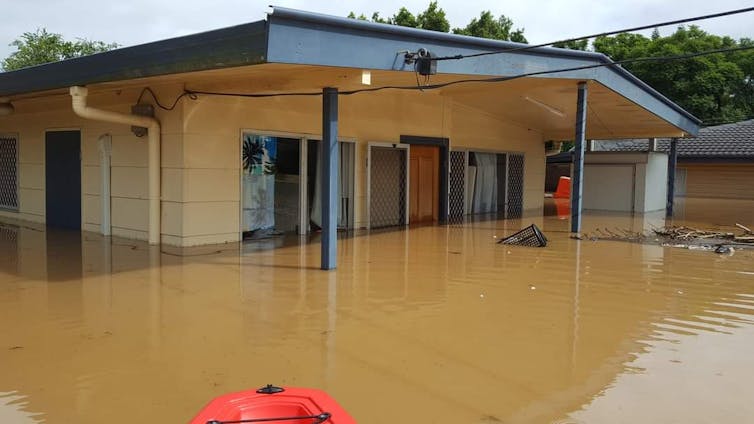 Brown floodwater almost engulfs a two-storey home in Goodna, Queensland, in February 2022. The water level is halfway up the door on the second level. View from a kayak.