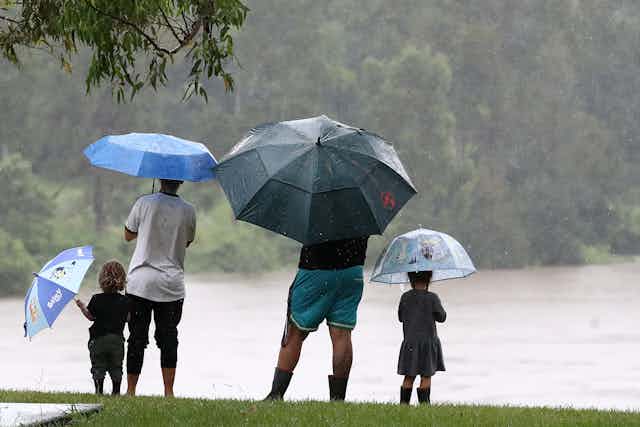 A family of four watches the rising river in the rain, holding umbrellas