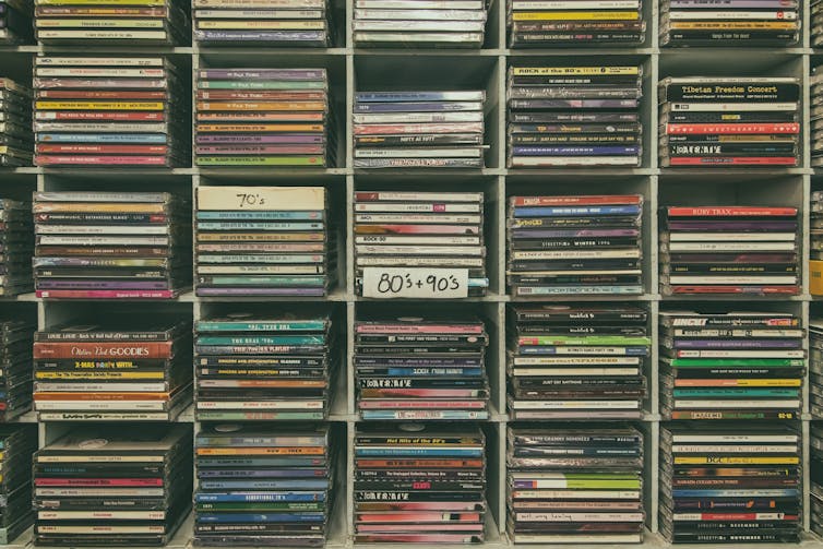 Secondhand compact discs from various decades displayed in a CD rack