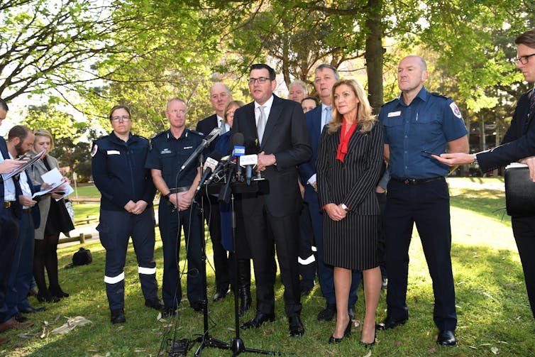 Premier Daniel Andrews, police officers and others address the media in a park