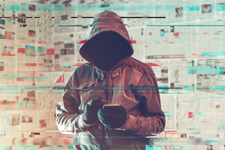 Hooded hacker person using smartphone in infodemic concept with digital glitch effect.