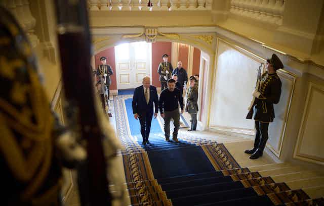 Ukrainian president, Volodymyr Zelensky, and US president, Joe Biden, walk up a carpeted flight of stairs flanked by Ukrainian guards.