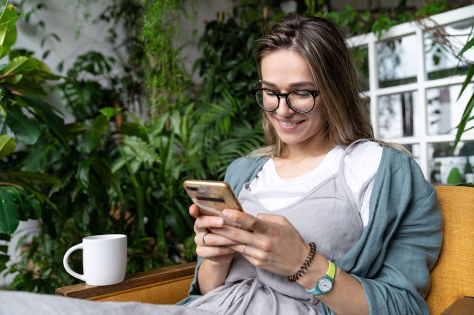 A woman smiling at her phone surrounded by houseplants.
