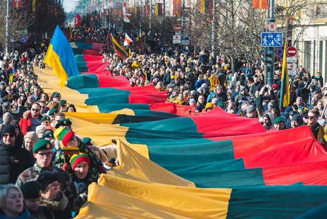Gigantesque drapeau lituanien porté par une foule, qui porte aussi un gros drapeau ukrainien