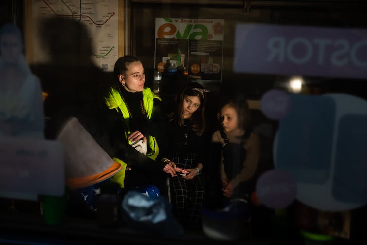 A woman with two children in a dark place that has a subway map behind it on the wall.