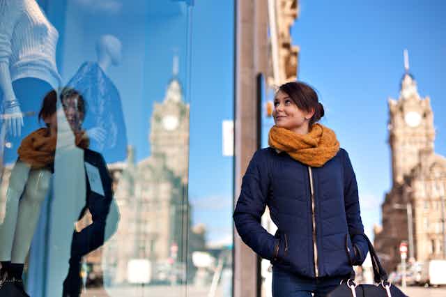 Woman looking at the clothes in a fashion store shop window, city backdrop, blue sky..