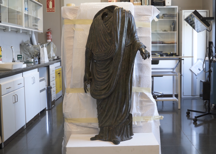 Imagen de una estatua togada sobre una caja de embalaje.