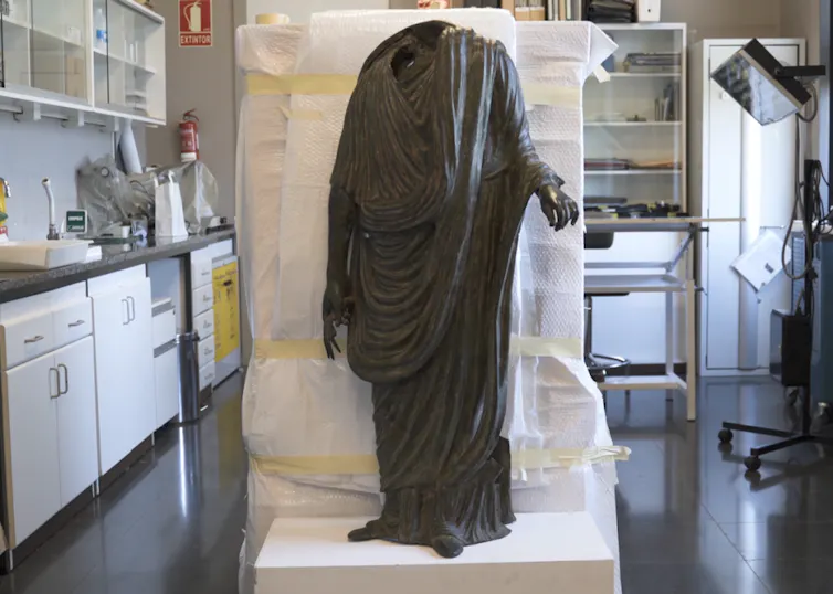 Imagen de una estatua togada sobre una caja de embalaje.