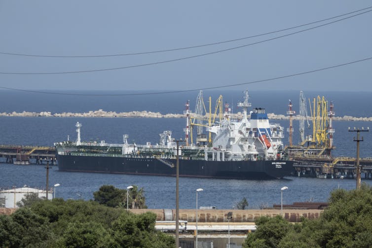 An oil tanker is moored at a dock near shore