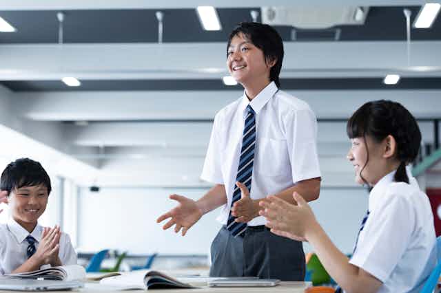 Three students in a classroom, applauding