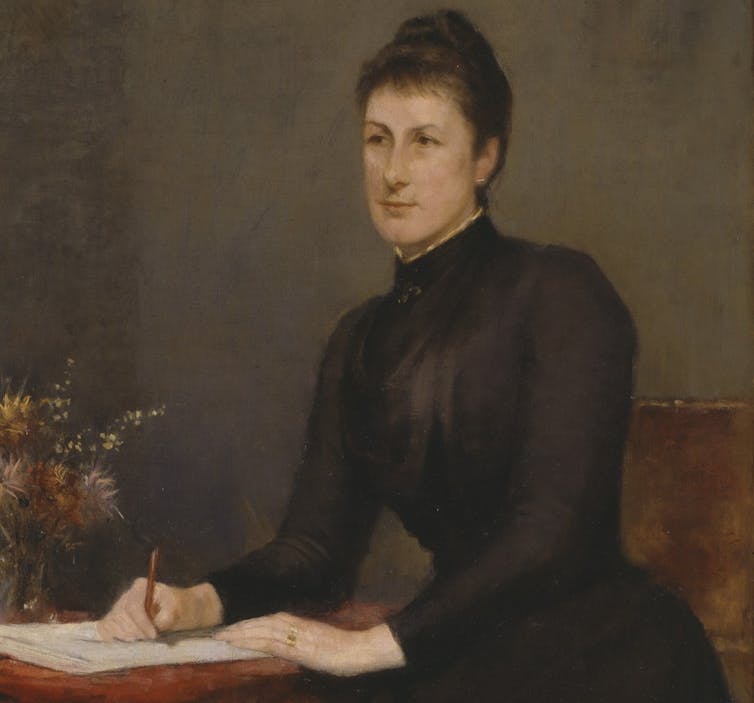 woman in bun and black dress at writing desk, with flowers