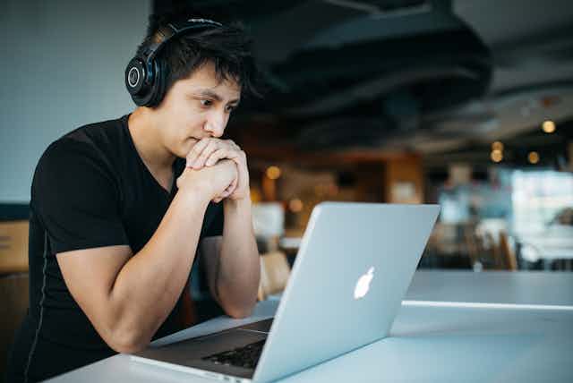 A man wearing headphones works at a laptop.