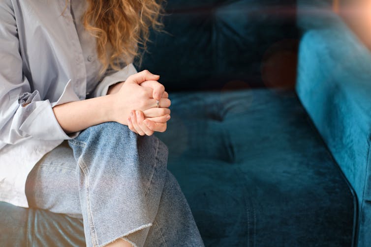 woman sits on couch with hands clasped