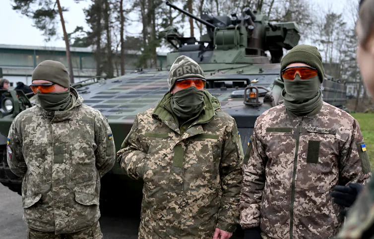 Three masked Ukrainian soldiers in front of a tank.