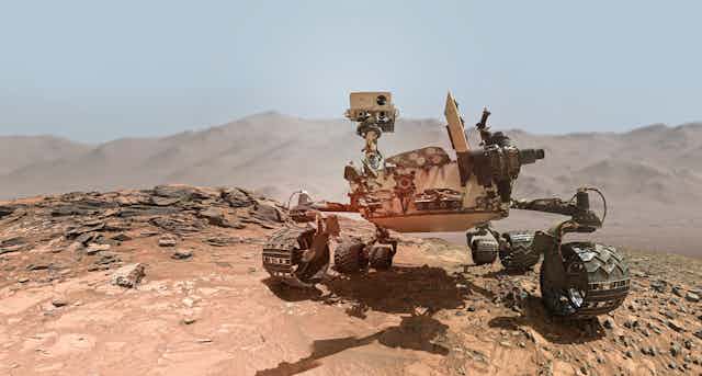 Photographic rendering of the Mars Curiosity rover in a red-dirt landscape. 