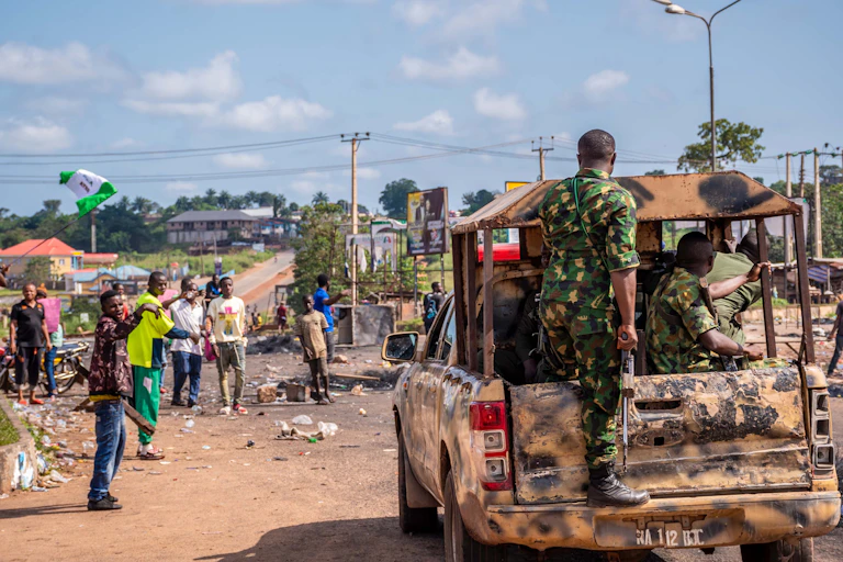 Nigerian protesters point their fingers at a truck carrying soldiers
