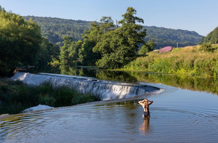 A swimmer standing in the shallows preparing to swim in the River Avon at Warleigh Weir in Somerset, England.
