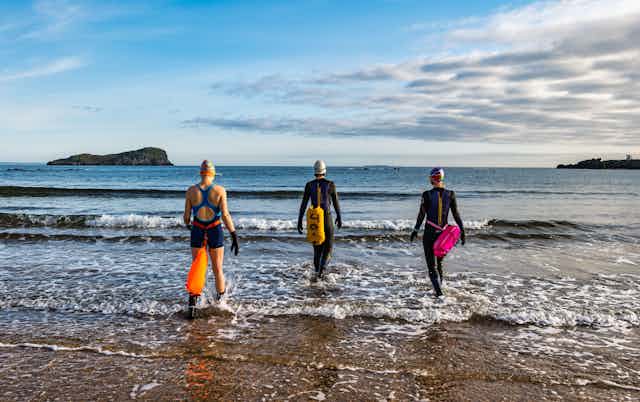 Open water women swimmers wearing wetsuits with buoyancy floats.