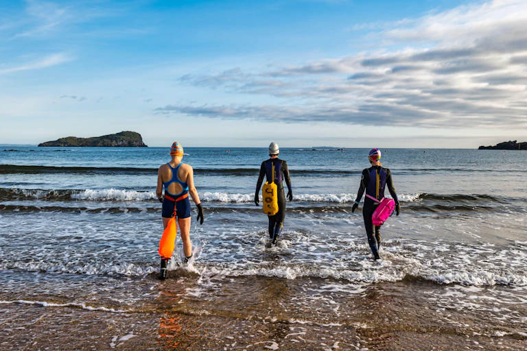 Open water women swimmers wearing wetsuits with buoyancy floats.