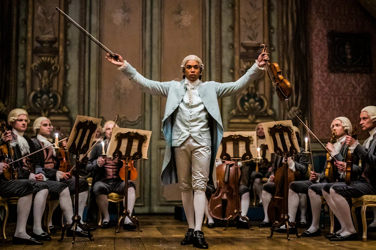 Un homme noir lève son violon et son archet parmi des violonistes blancs dans une scène d'un film d'époque.
